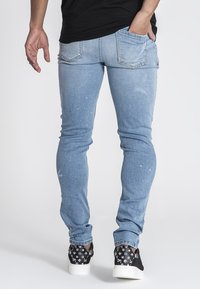 Ljusblå denimjeans med smal passform, som har subtila blekningar, färgfläckar och två bakfickor. Bärs med mönstrade svarta sneakers.