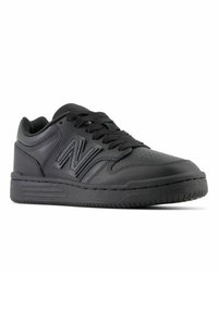 Schwarze Sportschuhe mit einem glatten Lederobermaterial, perforierter Zehenpartie und strukturiertem Gummisohle. Mit großem New Balance-Logo und flachen Schnürsenkeln.