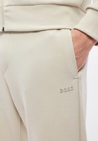 Jasnobeżowe spodnie dresowe wykonane z teksturowanego materiału posiadają boczne kieszenie oraz subtelne haftowane logo „BOSS” na udzie.