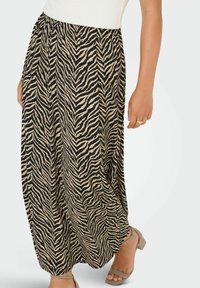 Maxi suknja od bež tkanine s crno-smeškastim uzorkom zebra, opuštenog kroja i gumiranim strukom. Uparena s bež sandalama na petu.