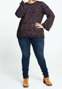 Kraftig svart tröja med flerfärgade fläckar, rund halsringning och långa ärmar, kombinerad med blå skinny jeans och tanfärgade klackboots.