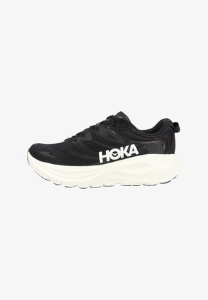Zapatilla de correr negra con suela blanca gruesa y gran logo "HOKA" en el lateral, diseño con cordones y cuello acolchado, vista de perfil.