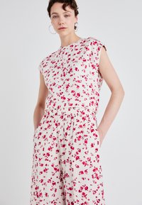Giubbotto floreale con un tessuto leggero e testurizzato color crema, caratterizzato da motivi di fiori rosa, maniche a cappuccio e una vita elastica con tasche.