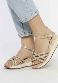 Sandalias de cuña beige con diseño de tiras cruzadas, textura metálica y una suela intermedia de estilo espadrille tejida, con suela de goma.