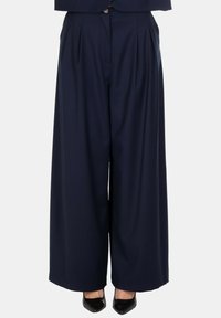 Pantaloni larghi a vita alta di colore navy con pieghe, indossati con scarpe nere con punta.
