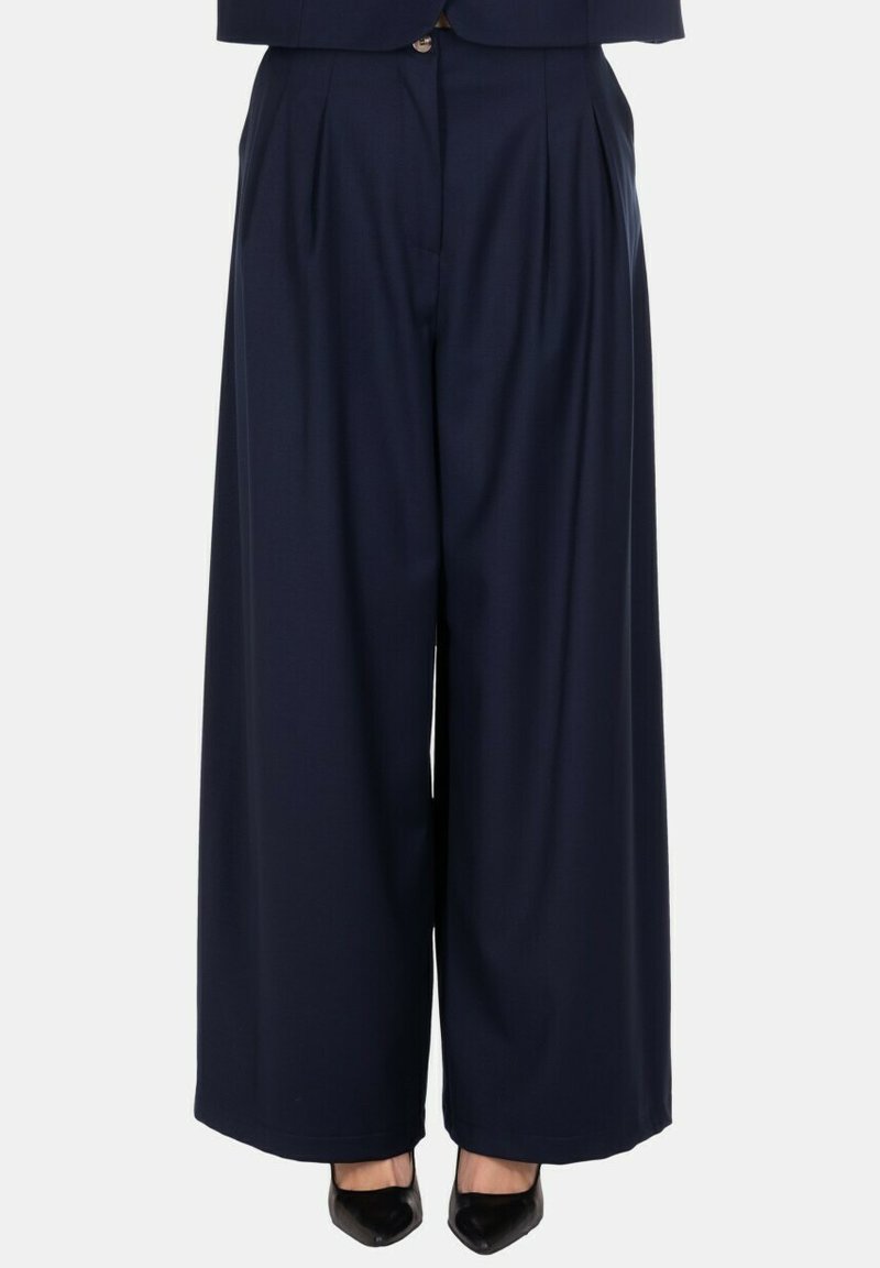 Pantaloni larghi a vita alta di colore navy con pieghe, indossati con scarpe nere con punta.