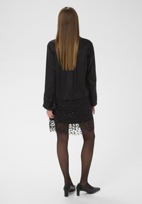 Crna bluza s ukrašenim rukavima, u kombinaciji s crnom suknjom od bisera. Prozirni sloj ima cvjetne uzorke, a upotpunjuju ga crne tajice i štikle.