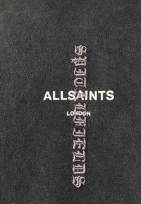 Sort tekstil med "ALLSAINTS" i hvid og "LONDON" nedenfor i mindre skrifttype, med en pink broderet vertikal tekstdesign.