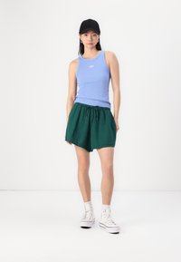 Canotta a coste di colore azzurro chiaro con il logo "GAP", abbinata a pantaloni corti verdi con cordino e sneakers alte bianche. Un cappellino nero completa il look.