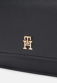 Mustapahvisettilompakko, jossa on kultasävyinen logo ja huomaamatonta ommeltua yksityiskohtaa. Liukas pinta ja tyylikäs, kompakti muotoilu.