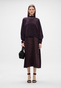 Ljubičasti oversized pulover s okruglim izrezom, uparen s lepršavom tamnoplavom suknjom. Crna torba i sandale s remenčićima zaokružuju izgled.