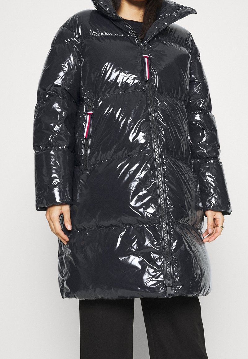 Svart puffig jacka med glänsande yta, med horisontella sömmar, hög krage och kontrasterande rosa dragkedjedetaljer. Långa ärmar och knälång design.
