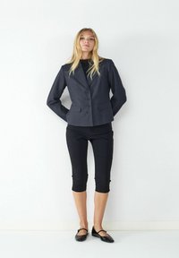 Navy pinstriped blazer with a fitted cut, two buttons, and side pockets, paired with black cropped pants and black flats.