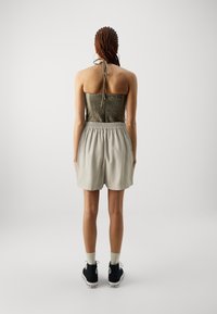 Bagfra af en person iført en stropløs, mørkegrøn top med en smocket design, parret med lysegrå shorts med elastisk talje og sorte sneakers.
