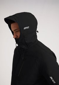 Giacca isolante nera con cappuccio, dotata di tasca frontale con zip, cordini regolabili e dettaglio del logo sul petto e sulla manica.