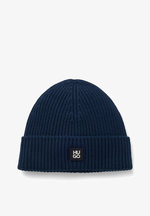 Dunkelblaue Strickmütze mit geripptem Muster, umgeschlagenem Saum und einem schwarzen rechteckigen Logo-Patch mit dem Aufdruck "HUGO". Weicher Stoff, simples Design.