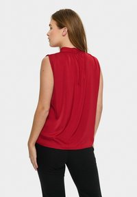 Top senza maniche rosso realizzato in tessuto liscio; presenta un collo arricciato e una vestibilità leggermente ampia. Sul retro ha un'apertura a chiave con un bottone.
