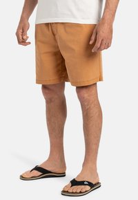 Pantalones cortos de algodón beige con corte recto, bolsillos laterales y un estilo casual. Combinados con chanclas negras que presentan un detalle de logo.