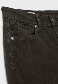 Pantalon en velours côtelé marron foncé en gros plan montrant la poche avant, les passants de ceinture, les coutures et les rivets en métal.