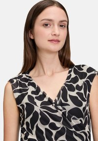 Robe sans manches présentant un décolleté en V, fabriquée en tissu léger avec une base crème et des motifs abstraits noirs. Design doux et drapé avec une poche.