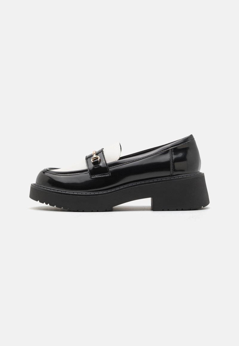 Mocassin en cuir verni noir et blanc avec une semelle épaisse et un détail boucle dorée sur un fond uni.