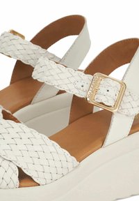 Witte gevlochten leren sandalen met twee banden, voorzien van een gouden vierkante gesp en een gevoerde beige binnenzool op een dikke witte zool.