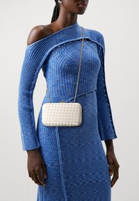 Gewebte metallene Clutch in Creme mit rechteckiger Form und Druckverschluß, kombiniert mit einem blau gerippten Kleid mit schulterfreiem Design und Knopfdetails.