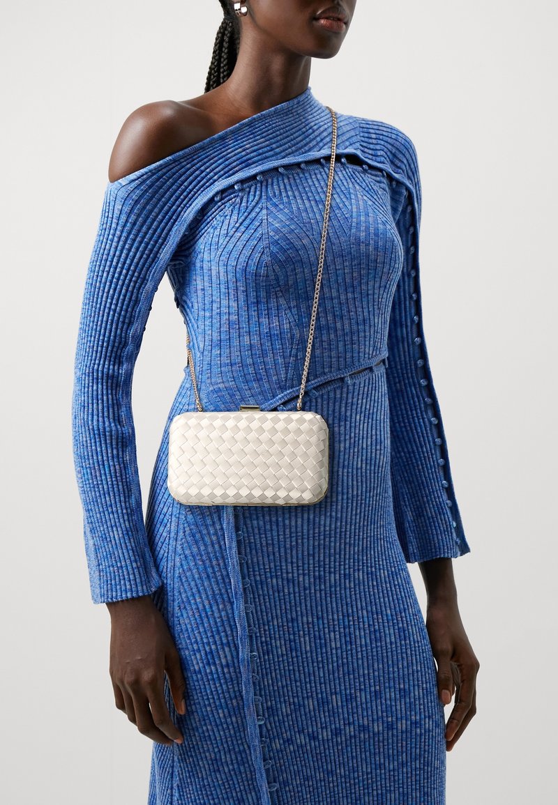 Gewebte metallene Clutch in Creme mit rechteckiger Form und Druckverschluß, kombiniert mit einem blau gerippten Kleid mit schulterfreiem Design und Knopfdetails.