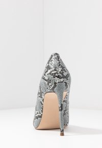 Chaussure à talon haut avec un design en serpent texturé gris et noir, bout pointu et talon aiguille avec une semelle nude.