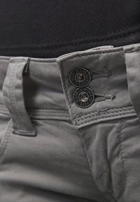 Grå denimbyxor med en slät textur. Funktioner två svarta knappar med ingraverad märkning, stabil sömnad och detalj vid midjan.