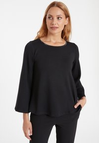 Schwarzes Langarmoberteil mit rundem Halsausschnitt und lässiger Passform. Hergestellt aus weichem Stoff, mit glatter Textur und subtiler Glanz entlang des Halsausschnitts.