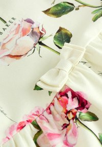 Virágmintás szövet, krémszínű alapon rózsaszín és lila rózsákkal; egy kis fehér masni díszíti a begyűrt anyagnál.
