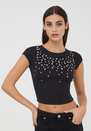 Top corto a coste nero con maniche corte, caratterizzato da decorazioni in strass sparse sulla parte frontale per un effetto decorativo.