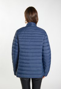 Giacca puffer blu navy con cuciture orizzontali, colletto alto e una texture liscia e lucida. La vista posteriore mostra assenza di tasche o elementi metallici visibili.