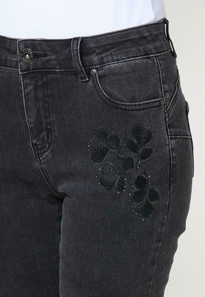 Jean en denim noir avec un design de broderie florale sur la cuisse gauche, agrémenté de petits strass. Style classique à cinq poches.