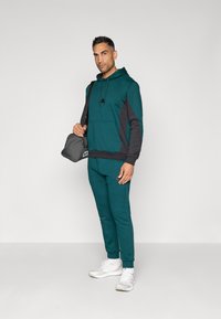 Teal kapuca z črnimi detajli, kenguru žep in vrvica. Teal jogging hlače in bele superge. Siva torba z logotipom.