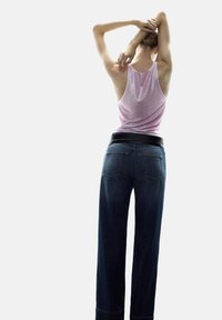 Camiseta de tirantes ajustada en un suave color rosa con una textura brillante, combinada con unos vaqueros de pierna ancha en azul oscuro que cuentan con un cinturón negro y dos bolsillos traseros.