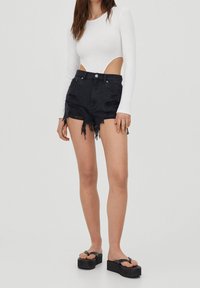 Bodysuit blanco de manga larga con laterales descubiertos, combinado con pantalones cortos de mezclilla negros desgastados con dobladillos deshilachados. Usado con sandalias de plataforma negras.