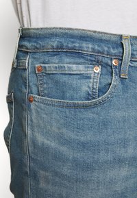 Light blue denim jeans with a faded texture, featuring copper-tone hardware, standard pockets, and a straight cut design.