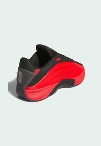 Black and red athletic shoe with a smooth, textured upper, curved silhouette, perforated detailing, and distinctive heel tab.