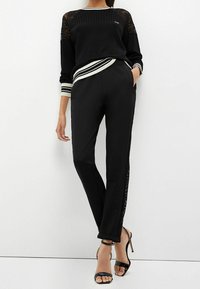 Czarny sportowy zestaw składający się z prążkowanego swetra z koronkowymi ramionami, paskowanymi mankietami oraz zwężanych spodni z koronkowymi panelami po bokach.