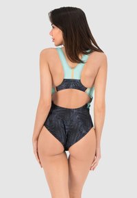 Maillot de bain une pièce avec un haut turquoise clair au design dos nageur, un bas noir avec un motif de feuille de palmier, et une découpe à l'arrière.