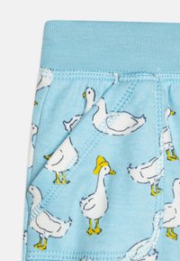 Blaues Material mit einem Muster aus weißen Enten, die gelbe Hüte tragen. Hat eine weiche Textur und einen elastischen Bund mit Nähdetails.