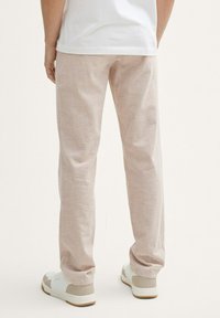Pantalones beige claros con un acabado texturizado, de corte ajustado y dobladillo vuelto, combinados con zapatillas blancas con acentos beige.