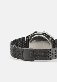 Montre en métal noir avec un boîtier octogonal et un bracelet en design tissé. Comprend une boucle marquée "CASIO" et un fond argenté.