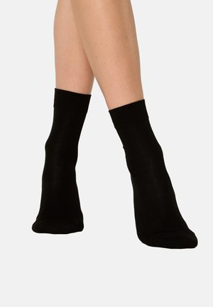 Schwarze Baumwollknöchelsocken mit glatt strukturiertem Material und gerippten Bündchen, die barfuß getragen werden und ein einfaches sowie funktionales Design zeigen.