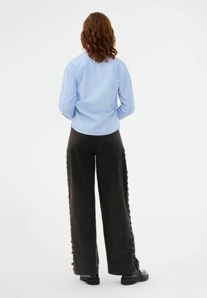 Lyseblå skjorte med knapper og sorte bukser med høj talje og knapper i siden. Outfitet har vide ben og sorte plateau-sko.