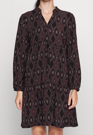 Schwarzes Kleid mit einem geometrischen Rautenmuster in Rot und Weiß. Verfügt über lange Ärmel, einen V-Ausschnitt und ein ausgestellt geschnittenes Rockdesign.