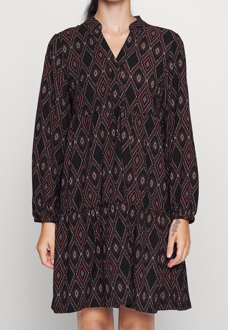 Svart klänning med ett geometriskt diamantmönster i rött och vitt. Har långa ärmar, V-hals och en utsvängd kjoldesign.