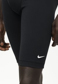 Gros plan d’une personne portant un short de compression sportif noir Nike avec un logo Nike swoosh blanc sur la cuisse gauche.